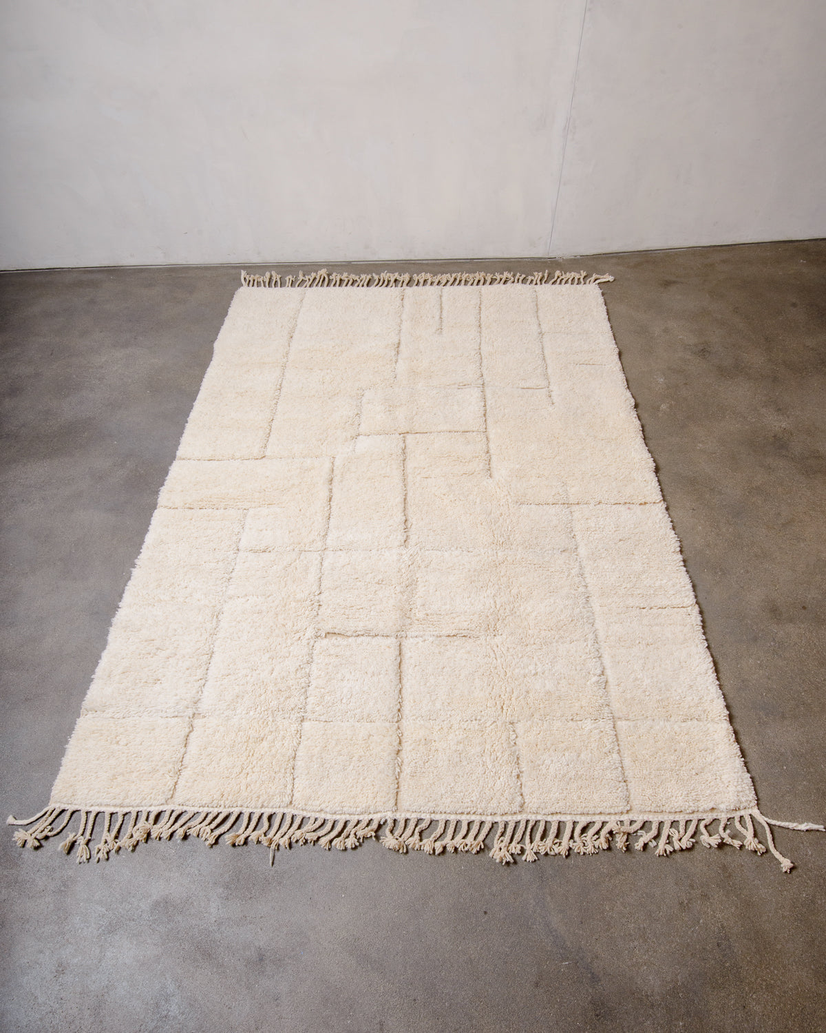 Berberlin Beniourain rug made of cream wool with minimal line design laying flat on concrete floor.